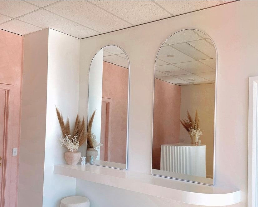 Two white arch mirrors with aluminium frame, hung to the wall in a hairdressing salon