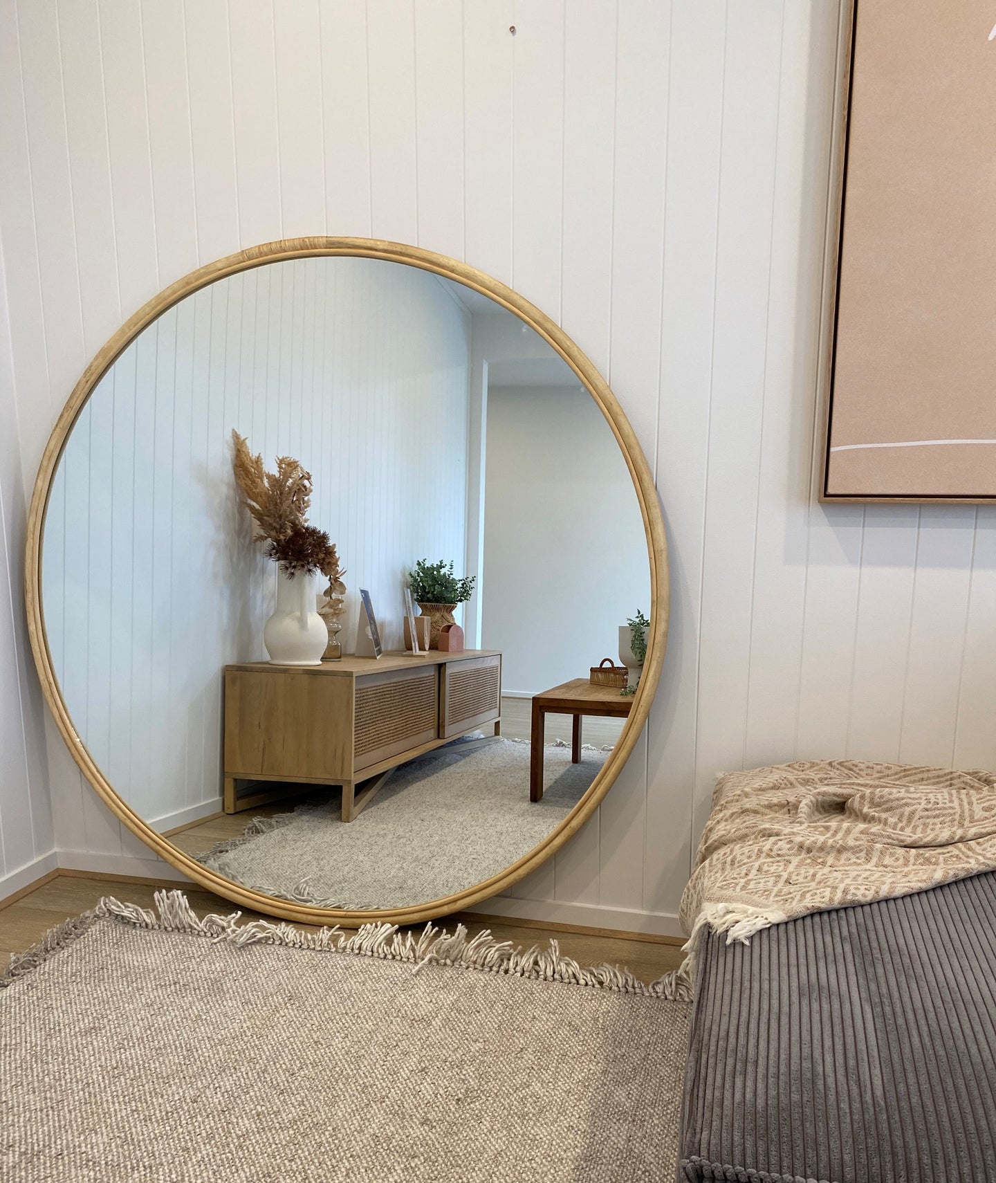 Large circle natural rattan mirror 1500mm in diameter, leaning against a white panelled wall in a newly built home